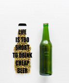 Draufsicht auf eine Flasche Bier in der Nähe von gepresstem Hopfen mit Leben ist zu kurz, um billiges Bier zu trinken Schriftzug isoliert auf weiß 