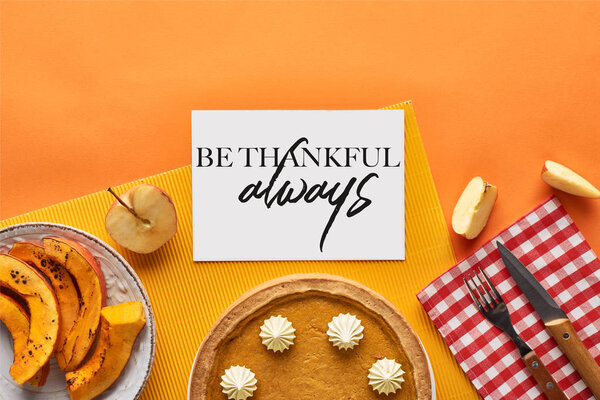 top view of delicious pumpkin pie near card with be thankful always illustration on orange background with apples