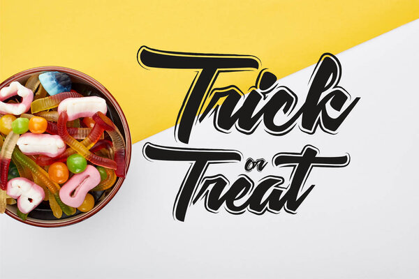 top view of colorful gummy sweets in bowl on yellow and white background with trick or treat illustration