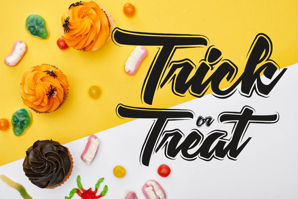 top view of colorful gummy sweets and cupcakes on yellow and white background with trick or treat illustration