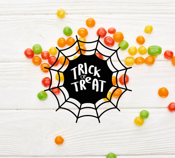 top view of colorful bonbons on white wooden table with spiderweb and trick or treat illustration