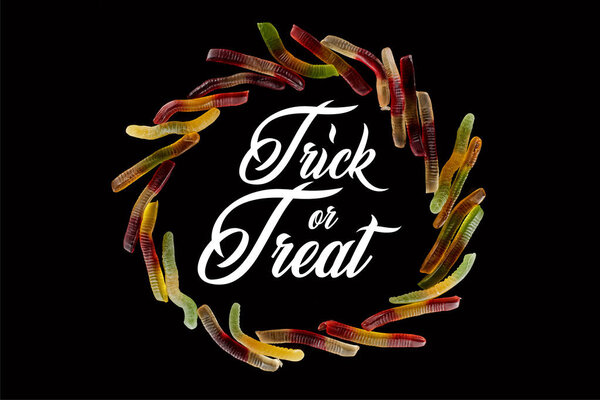 top view of round frame made of colorful gummy worms isolated on black with trick or treat illustration
