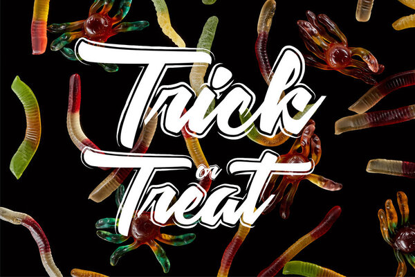 top view of colorful gummy spiders and worms isolated on black with trick or treat illustration