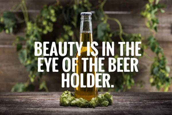 fresh beer in bottle with green hop on wooden surface with beauty is in the eye of the beer holder illustration