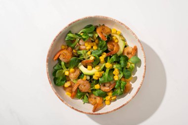 Beyaz arka planda taze yeşil salata, mısır, karides ve avokado tabağı.