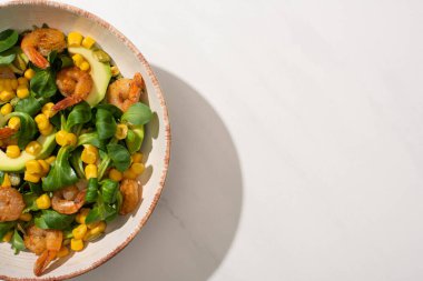 Beyaz arka planda taze yeşil salata, mısır, karides ve avokado tabağı.
