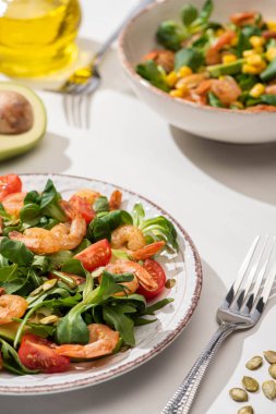 Karidesli taze yeşil salata ve beyaz arka planda çatalların yanındaki tabaklarda avokado.