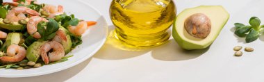 Beyaz arka planda zeytinyağının yanında karides ve avokado kaplı taze yeşil salata, yatay görüntü