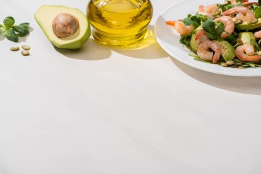 Beyaz arka planda zeytinyağının yanında karides ve avokado tabağında taze yeşil salata.
