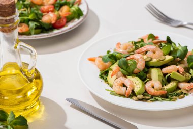 Taze yeşil salata, karides ve avokado tabakta zeytinyağı ve beyaz arka planda çatal bıçak.