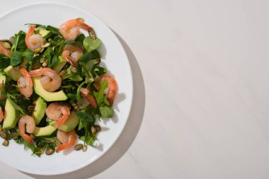 Beyaz zemin üzerinde balkabağı tohumları, karides ve avokado ile taze yeşil salata manzarası