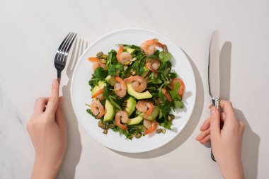 Beyaz arka planda balkabağı çekirdeği, karides ve avokado ile taze yeşil salata yiyen kadının kısmi görüntüsü
