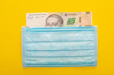 Sarı arka planda Ukrayna banknotu ve tıbbi maskesinin üst görüntüsü