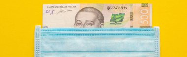 Sarı zemin üzerinde Ukrayna banknotu ve tıbbi maske, panoramik çekim