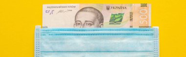 Sarı zemin üzerinde Ukrayna banknotu ve tıbbi maske, panoramik çekim