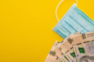 Sarı arka planda Ukrayna banknotlarının ve tıbbi maskenin üst görüntüsü