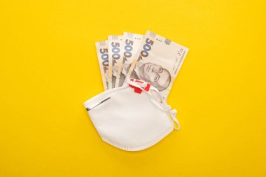 Sarı arka planda Ukrayna banknotları ve güvenlik maskesi üst görünümü