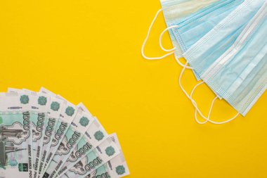 KYIV, UKRAINE - 25 Mart 2020: Sarı arka planda Rus banknotlarının ve tıbbi maskelerin üst görüntüsü