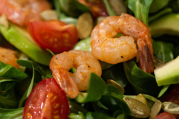 close up view of fresh green salad with pumpkin seeds, cherry tomatoes, shrimps and avocado