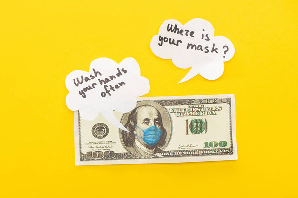КИЕВ, УКРАИНА - 25 МАРТА 2020 г.: вид сверху банкноты доллара с нарисованной медицинской маской рядом с речевыми пузырями на желтом фоне
