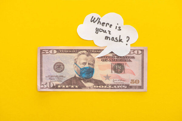 КИЕВ, УКРАИНА - 25 МАРТА 2020 г.: вид сверху на банкноту доллара с нарисованной медицинской маской и речевым пузырем на желтом фоне
