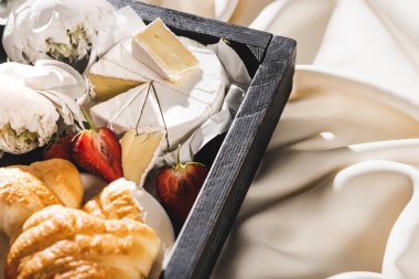 Fransız kahvaltısını kruvasan, Camembert, ahşap tepside çilek, desenli beyaz kumaş ve şakayık.