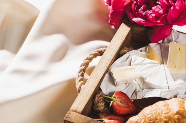 Fransız kahvaltısını kruvasan, Camembert, ahşap tepside çilek, desenli beyaz kumaş ve şakayık.