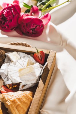 Fransız kahvaltısını kruvasan, Camembert, ahşap tepside çilek, desenli beyaz kumaş ve şakayık.