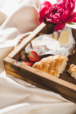 Fransız kahvaltısını kruvasan, Camembert, ahşap tepside çilek, desenli beyaz kumaş ve şakayık.