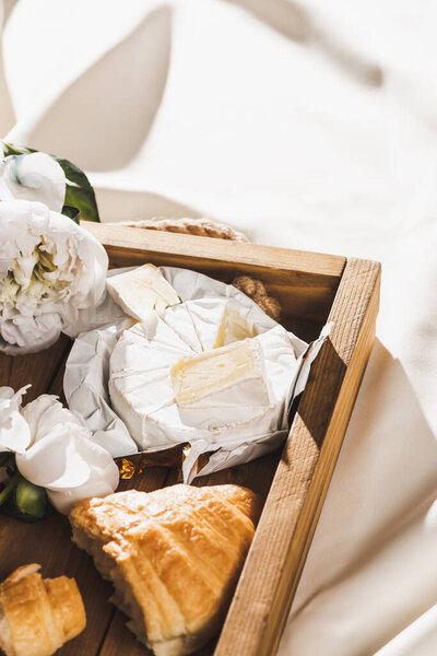 close up view of french breakfast with croissant, Camembert on wooden tray on textured white cloth with peony