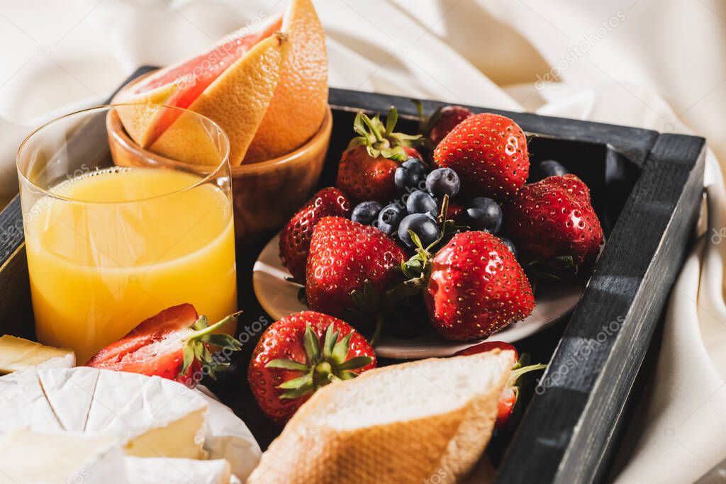 close up view of french breakfast with grapefruit, Camembert, orange juice, berries and baguette on wooden tray