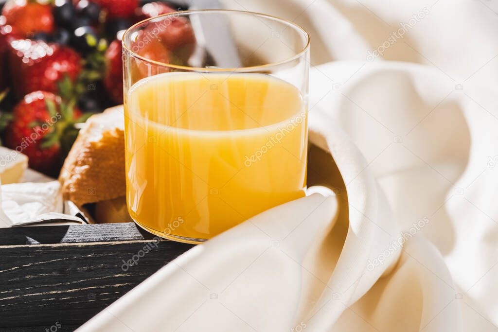 close up view of french breakfast with orange juice, berries on wooden tray on textured white cloth