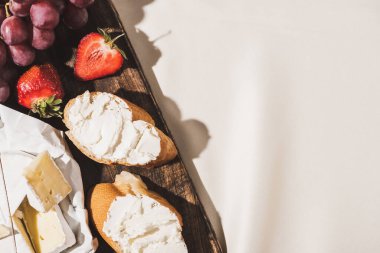 Fransız kahvaltısının baget, Camembert, çilek ve üzümlü beyaz masa örtüsünün üzerindeki tahta kesme tahtasının üst görüntüsü.