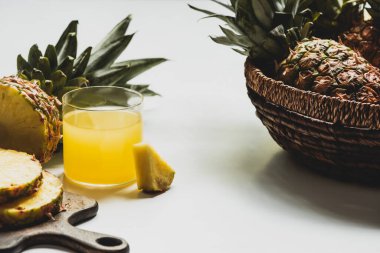 Taze ananas suyu, ahşap kesim tahtasında lezzetli meyvelerin yanında ve beyaz arka planda kasede.