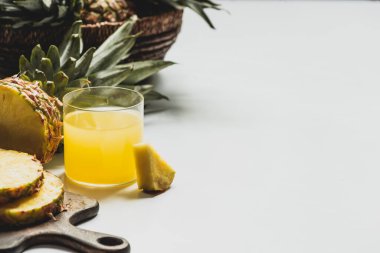 Taze ananas suyu, beyaz arka planda ahşap kesim tahtasındaki lezzetli meyvelerin yanında.