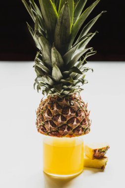 Bardakta taze ananas suyu. Siyah üzerine izole edilmiş beyaz yüzeyde lezzetli meyveler.
