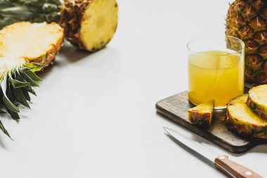 Bardakta taze ananas suyu, beyaz arka planda bıçakla ahşap kesme tahtasındaki lezzetli meyvelerin yanında.