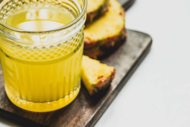 Bardaktaki taze ananas suyunun seçici odağı beyaz arka plandaki ahşap kesme tahtasındaki lezzetli meyve.