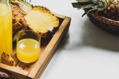 Taze ananas suyu ve ahşap tepside lezzetli meyve ve beyaz arka planda sepet.