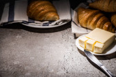 selektivní zaměření čerstvých pečených croissantů na ručník u másla a nůž na betonovém šedém povrchu v tmavé