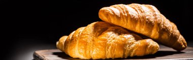 fresh baked croissants on wooden cutting board isolated on black, panoramic shot clipart