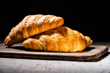 fresh baked croissants on wooden cutting board on concrete grey surface isolated on black clipart