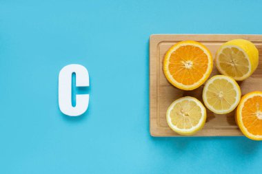 top view of ripe cut lemon and orange on wooden cutting board near letter C on blue background clipart
