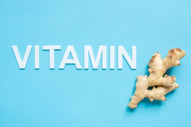 top view of ginger root and word vitamin on blue background clipart