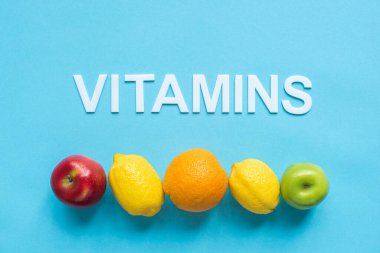 Olgun meyvelerin en üst görünümü sırada ve mavi arkaplanda kelime vitaminleri