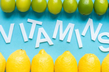 Mavi zemin üzerinde olgun sarı limon ve limonların kelime vitaminleriyle üst görünümü