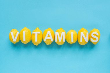 Olgun sarı limonların ve mavi arka planda kelime vitaminlerinin üst görüntüsü