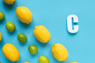 Olgun sarı limonlar, yeşil limonlar ve mavi arka planda C harfi ile düz yatıyordu.