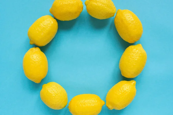 蓝色背景的圆形空框架中的成熟的黄色柠檬的顶部视图 — 图库照片