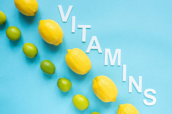 flat lay with ripe yellow lemons, green limes and word vitamins on blue background
